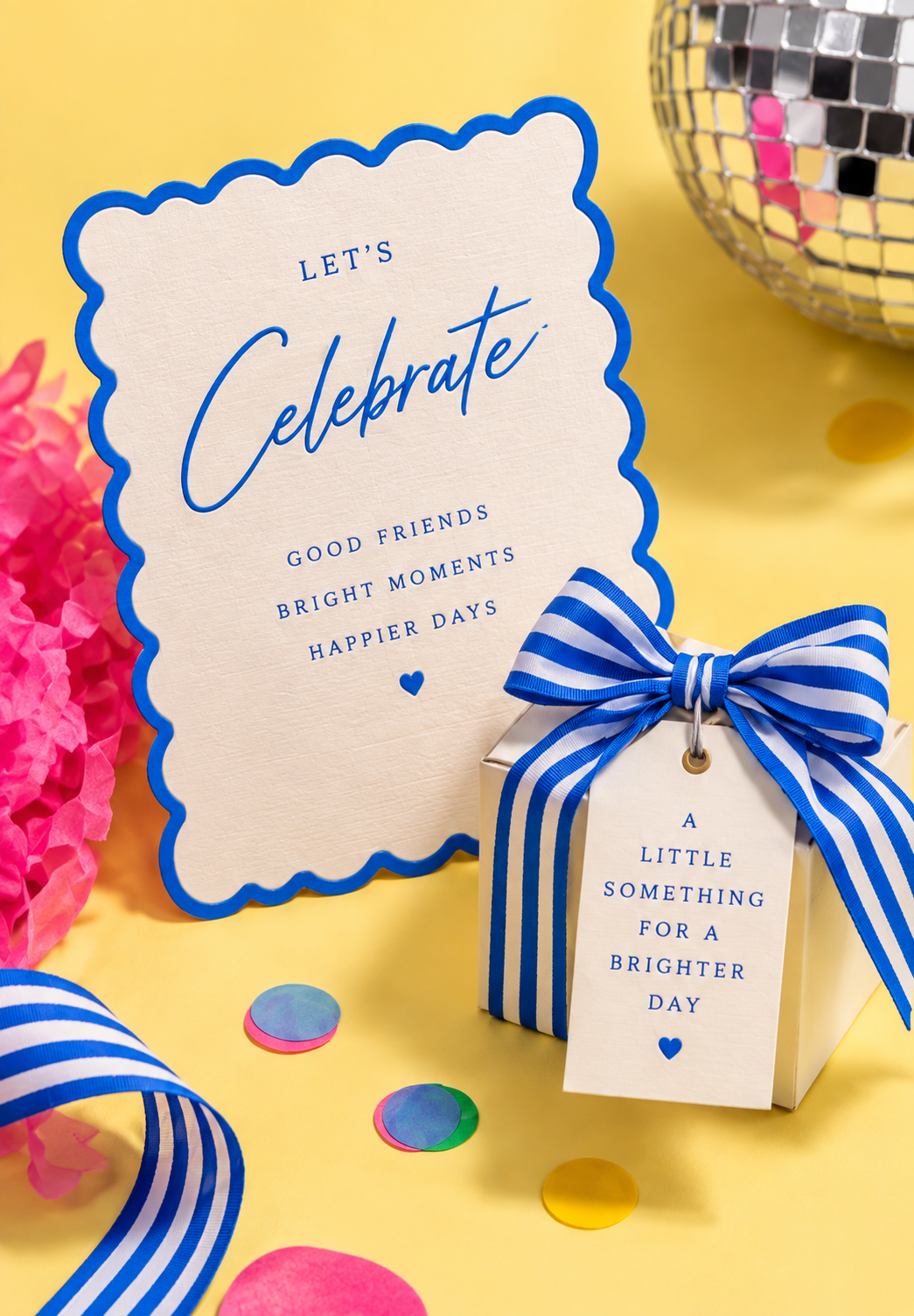 A blue scalloped invitation and striped ribbon favor box on a sunny yellow background