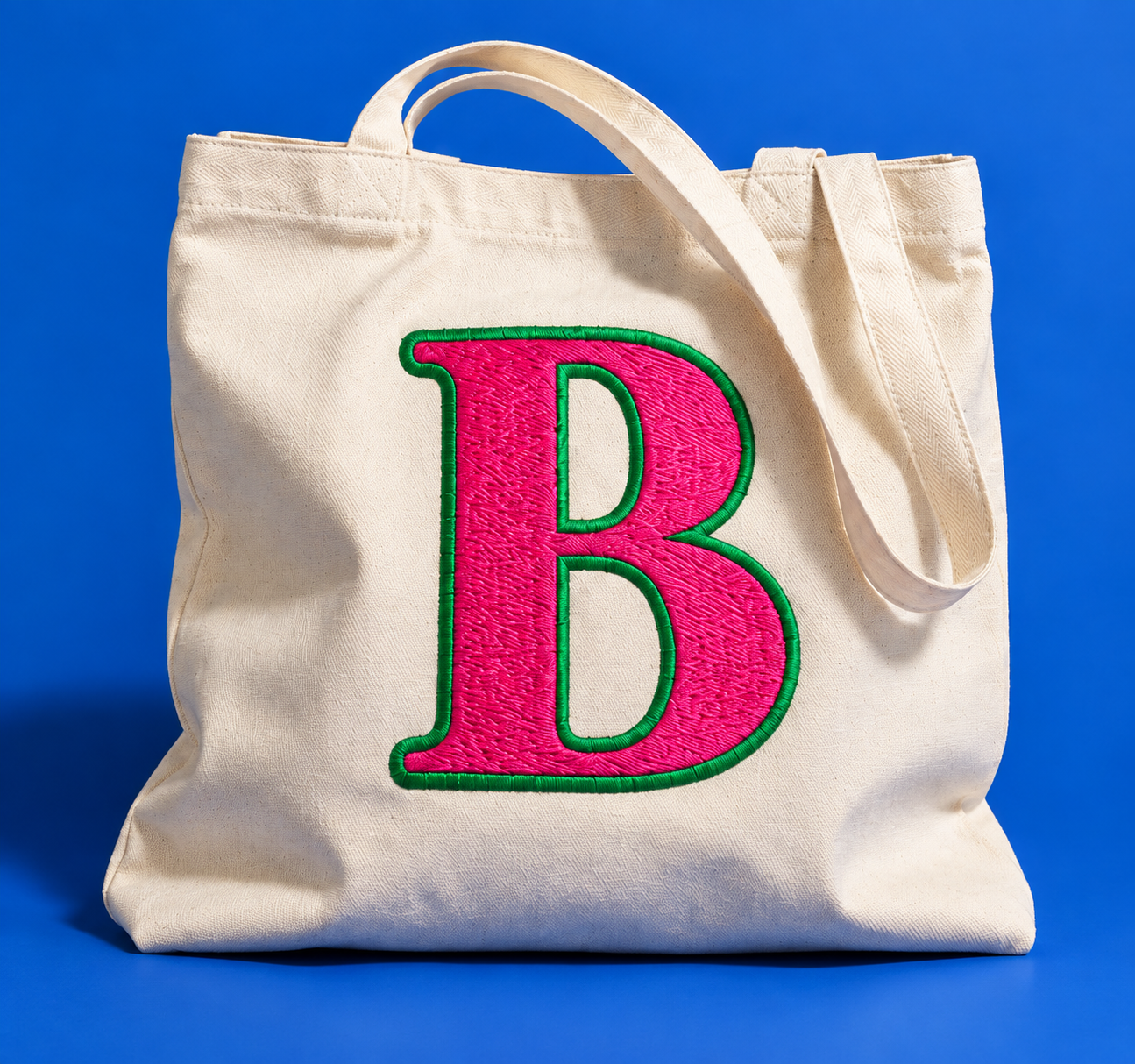 Cream canvas tote with a large pink B edged in green embroidery on a cobalt background